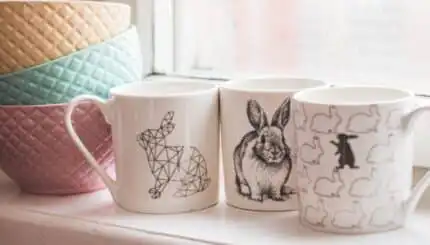 Set de căni personalizate cu design minimalist, ilustrând iepuri stilizați, așezate pe pervazul unei ferestre.